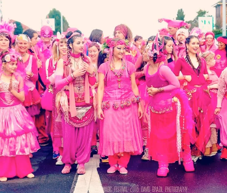 large group of dancers in elaborate bright pink costumes in a line, smiling, getting ready